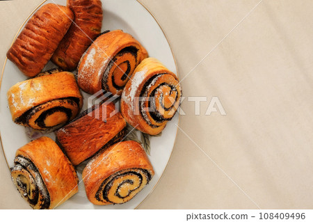 Buns with poppy seeds on a plate on a beige background. Sweet homemade bun. Top view. Buns with poppy seeds on a plate on a beige background. Sweet homemade bun. Top view. 108409496