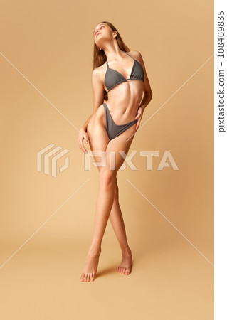 Charming beautiful woman with with perfect shape and long brunette hair posing in lingerie, swimsuit isolated sand color background. Charming beautiful woman with with perfect shape and long brunette hair posing in lingerie, swimsuit isolated sand color background. 108409835