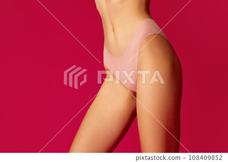 Cropped perfect sporty body shape female body dressed in sensual pink lingerie against vivid red studio background. Concept of dieting. 108409852