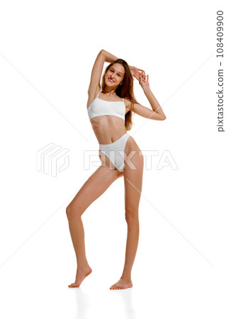 Full length portrait of Slim Caucasian 20s lady posing in white under wear with hands raised up, showing her ideal curves. Full length portrait of Slim Caucasian 20s lady posing in white under wear with hands raised up, showing her ideal curves. 108409900