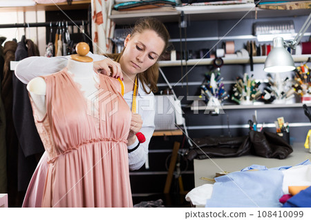 Woman professional sewer measuring dress at mannequin workshop Woman professional sewer measuring dress at mannequin workshop 108410099
