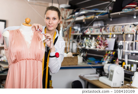 Female seamstress is thinking about new dress for collection of clothes near mannequin 108410109