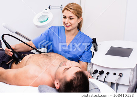 Qualified woman cosmetologist with male client during hardware body procedure in modern aesthetic clinic 108410158