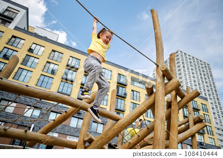 A girl hangs on a rope from a wooden sports complex. 108410444