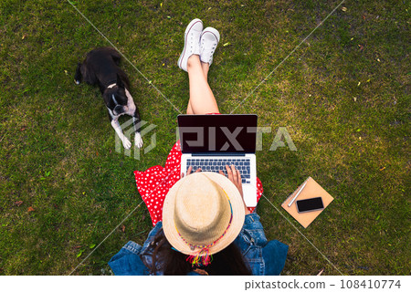 Top view of young woman sitting on grass with her dog and using laptop 108410774