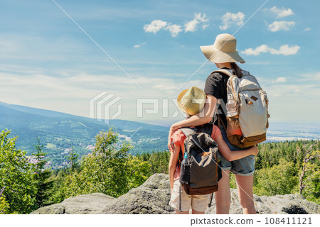 Back view of young two girls with backpacks standing on top of a mountain and looking at the valley Back view of young two girls with backpacks standing on top of a mountain and looking at the valley 108411121