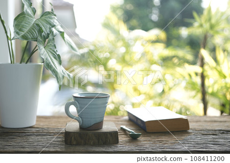 Coffee mug and old book and plant pot on weathered wooden table 108411200