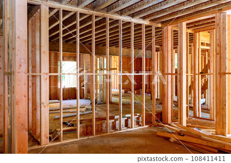 Interior of new unfinished house under construction with wooden framing beams to walls Interior of new unfinished house under construction with wooden framing beams to walls 108411411