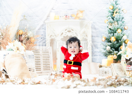 A smiling 1-year-old baby wearing Santa's clothes and having fun with the Christmas tree 108411743