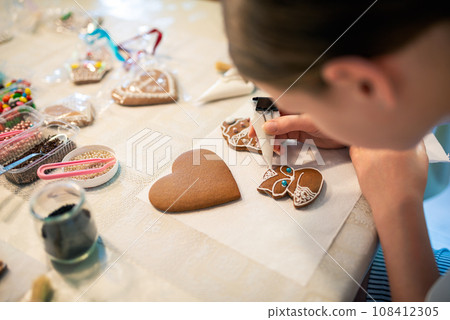Close-up of a young girl decorating gingerbread cookies with icing. Close-up of a young girl decorating gingerbread cookies with icing. 108412305