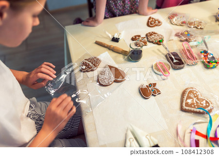 Culinary workshops. Children decorating gingerbread cookies with glaze on table at home Culinary workshops. Children decorating gingerbread cookies with glaze on table at home 108412308