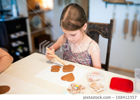 Culinary workshops for children and gingerbread decorating. Young girl decorating gingerbread cookies in the shape of a heart, a fox and a cupcake 108412357