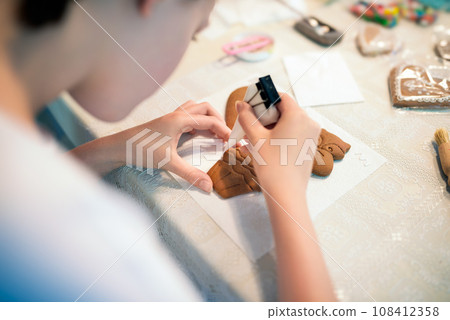 Close-up of a young woman decorating gingerbread cookies with icing. 108412358
