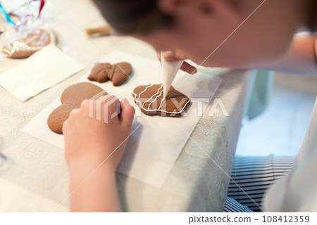 Girl decorating gingerbread cookies with icing sugar. Selective focus. 108412359