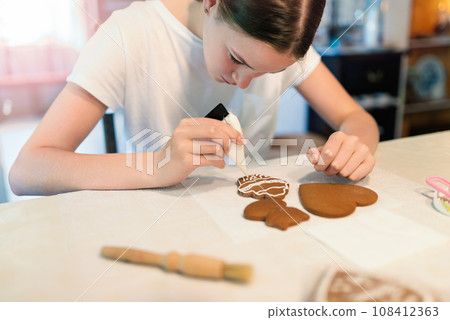 Girl decorating gingerbread cookies with icing sugar. Selective focus. 108412363