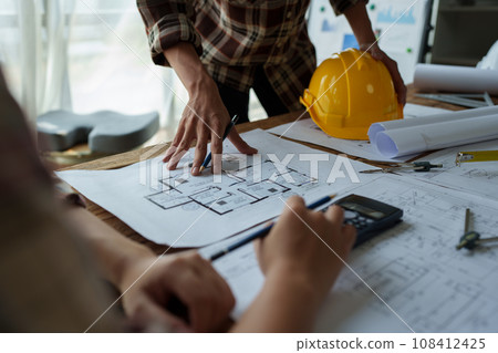 multi ethnic engineer brainstorming and measuring for cost estimating on blueprint and floor plan drawings about design architectural and engineering for houses and buildings. 108412425
