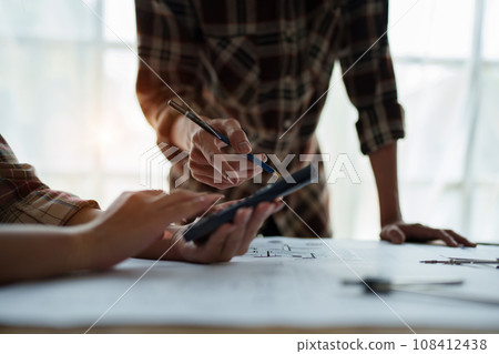 multi ethnic engineer brainstorming and measuring for cost estimating on blueprint and floor plan drawings about design architectural and engineering for houses and buildings. 108412438