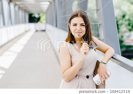 Happy young business woman holding mobile phone while walking on the street. 108412519