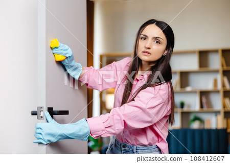 A young pretty woman in rubber gloves wipes the door with a rag 108412607