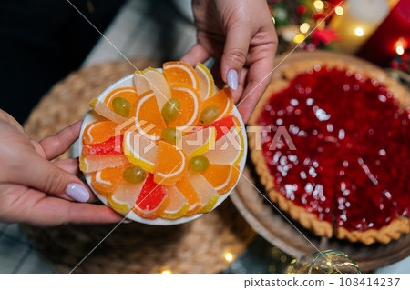 Close-up top view of unrecognizable young woman putting plate with delicious marmalade on served table during prepare family party. Concept of preparation home to new year holiday celebration. 108414237
