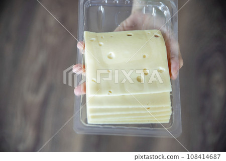 A woman's hand takes a piece of cheese from a pack close-up. Preparing for Cheese Lovers Day. A woman's hand takes a piece of cheese from a pack close-up. Preparing for Cheese Lovers Day. 108414687