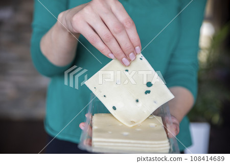 A woman's hand takes a piece of cheese from a pack close-up. Preparing for Cheese Lovers Day. A woman's hand takes a piece of cheese from a pack close-up. Preparing for Cheese Lovers Day. 108414689