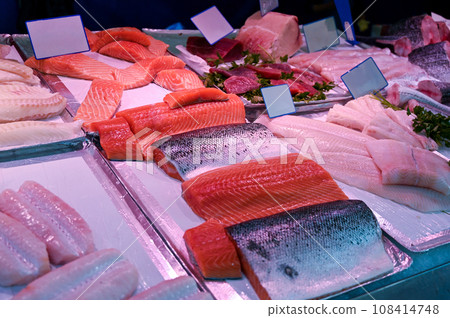 Nice fish counter featuring vibrantly colored salmon fillets. Alongside fillets of other varieties of fish and some parsley leaves. Copy space on white cards. 108414748
