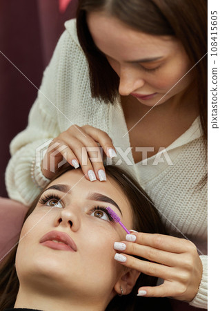 master combs the eyelashes of the client after the eyelash extension procedure. Cosmetology and skin care 108415605