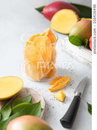 Dried mango in glass jar with raw fruits and knife on light board.Top view. Dried mango in glass jar with raw fruits and knife on light board.Top view. 108416496