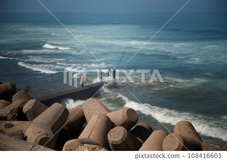 Rear view of unrecognizable people - fisherman standing on the seashore on breakwater and fishing in Atlantic Ocean. People. Leisure. Hobby 108416603