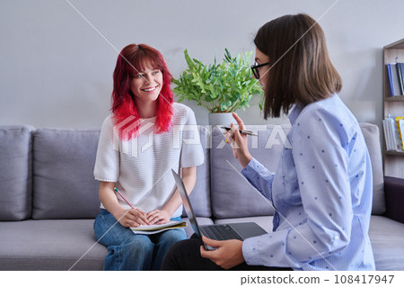 Teenage girl student talking with female teacher, sitting together in office 108417947