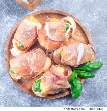 Prosciutto peach bruschetta. Crostini, cream cheese, basil, peach and prosciutto, square, top view 108420603