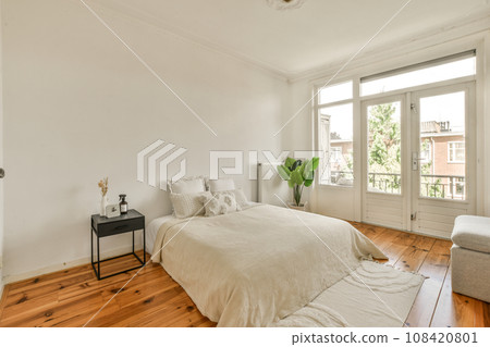 a bedroom with wood floors and white walls, including a bed in the center of the room there is a small table on the a bedroom with wood floors and white walls, including a bed in the center of the room there is a small table on the 108420801