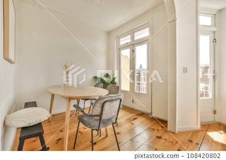 a dining table and chairs in a room with white walls, hardwood flooring and large windows looking out onto the street a dining table and chairs in a room with white walls, hardwood flooring and large windows looking out onto the street 108420802