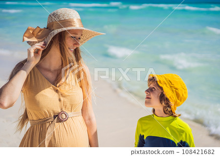 A radiant pregnant mother and her excited son share a tender moment on a serene, snow-white beach, celebrating family love amidst nature's beauty A radiant pregnant mother and her excited son share a tender moment on a serene, snow-white beach, celebrating family love amidst nature's beauty 108421682