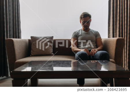Lonely man sits on the sofa thinking of his lover. Lonely man sits on the sofa thinking of his lover. 108421695