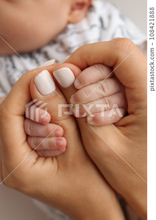 Parents' hands hold the fingers of a newborn baby. The hand of a mother and father close-up holds the fist of a newborn baby. Family health and medical care. Professional photo on white background 108421888