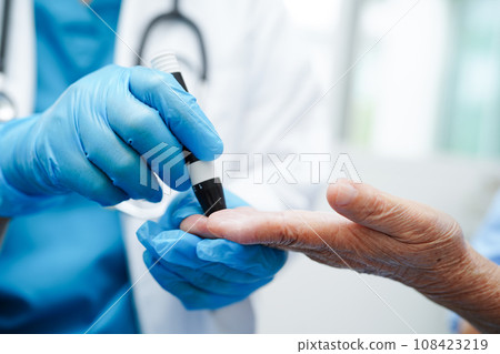 Asian doctor using lancet pen on senior patient finger for check sample blood sugar level to treatment diabetes.. 108423219