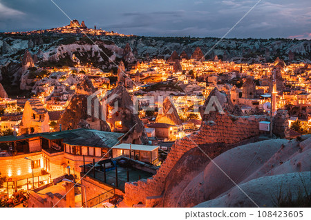 從土耳其旅遊勝地卡帕多西亞市中心的觀景台上可以看到奇異的岩層和發出橙色光芒的岩石住宅的美麗夜景。 108423605