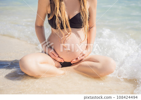 Radiant and expecting, a pregnant woman stands on a pristine snow-white tropical beach, celebrating the miracle of life against a backdrop of natural beauty 108424494