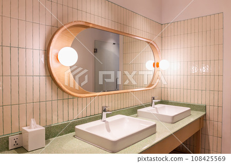 Wood-framed mirror in bathroom with lights and sink with silver faucet and socket. Wood-framed mirror in bathroom with lights and sink with silver faucet and socket. 108425569