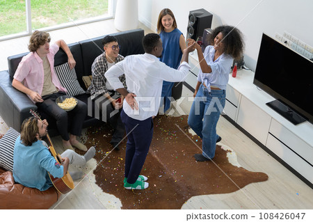 Multiethnic group of friends having fun at home. Young people dancing, playing guita and drinking wine in living room.. 108426047