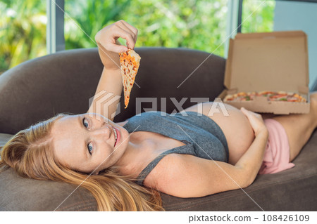 A pregnant woman enjoys a slice of pizza, savoring a moment of indulgence while satisfying her craving for a delightful, comforting treat. Excited Pregnant Young Lady Enjoying Pizza Holding Biting A pregnant woman enjoys a slice of pizza, savoring a moment of indulgence while satisfying her craving for a delightful, comforting treat. Excited Pregnant Young Lady Enjoying Pizza Holding Biting 108426109