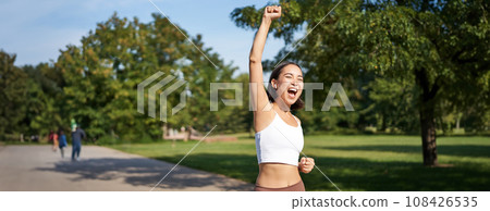 Hooray, victory. Smiling asian girl triumphing, celebrating achievement, running till finish, shouting from excitement 108426535