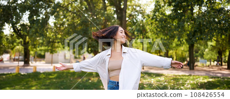 Freedom and people concept. Happy young asian woman dancing in park around trees, smiling and enjoying herself 108426554