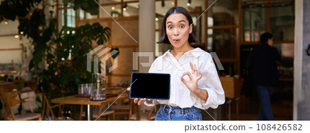 Enthusiastic asian woman shows okay sign, tablet screen, looks impressed, recommends smth 108426582