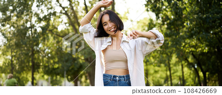 Carefree woman dancing and walking in park with hands lifted up high, smiling happily. Lifestyle concept Carefree woman dancing and walking in park with hands lifted up high, smiling happily. Lifestyle concept 108426669