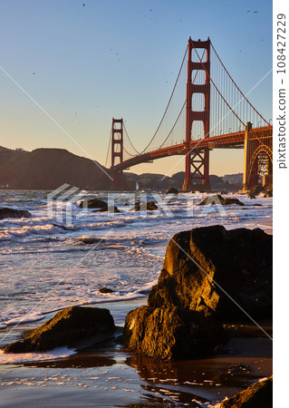 Wet sandy beach with giant boulders and distant Golden Gate Bridge at sunset Wet sandy beach with giant boulders and distant Golden Gate Bridge at sunset 108427229