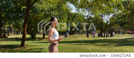 Active asian girl, in fitness clothing, workout in park, walking in sportswear with smartphone and water bottle Active asian girl, in fitness clothing, workout in park, walking in sportswear with smartphone and water bottle 108427248