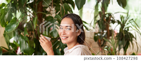 Vertical shot of young asian woman with digital tablet and graphic pen, drawing, scratching while sitting in cafe with cup of coffee 108427298